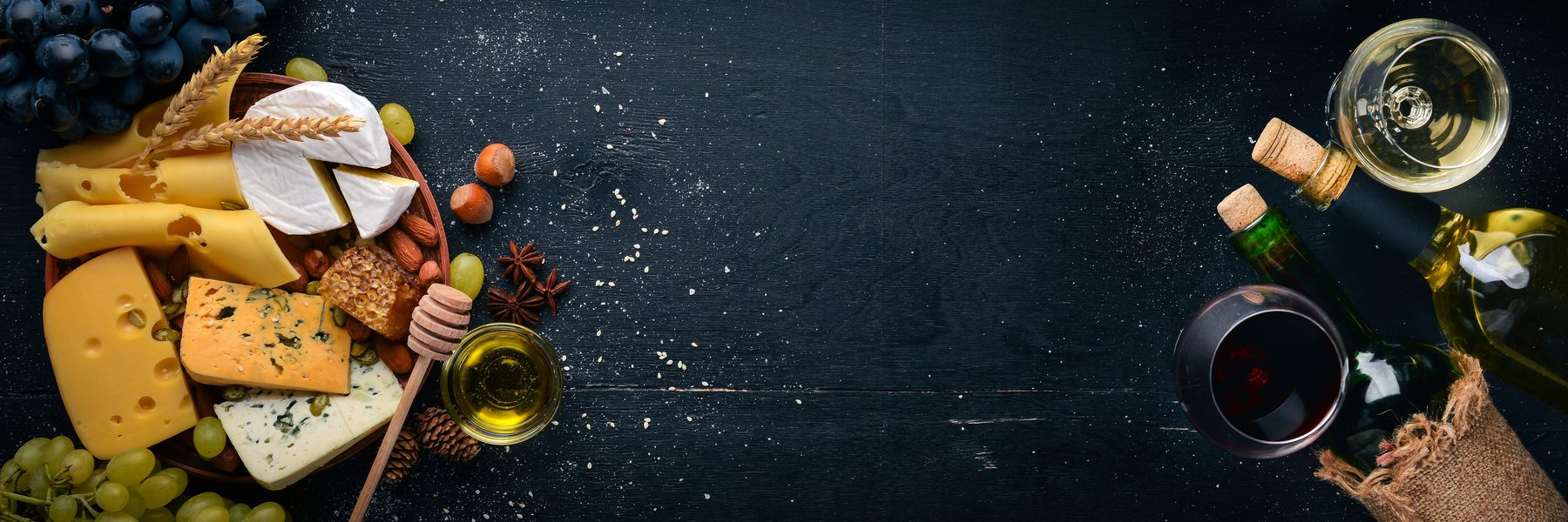 Olive oil, grapes and picnic provisions laid out on a dark table